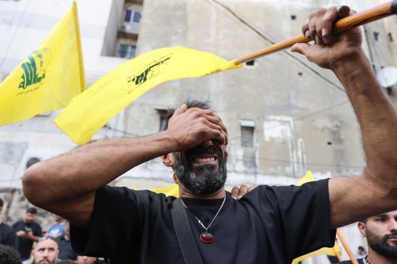 A man shields his face while grimacing and holding up a yellow flag.