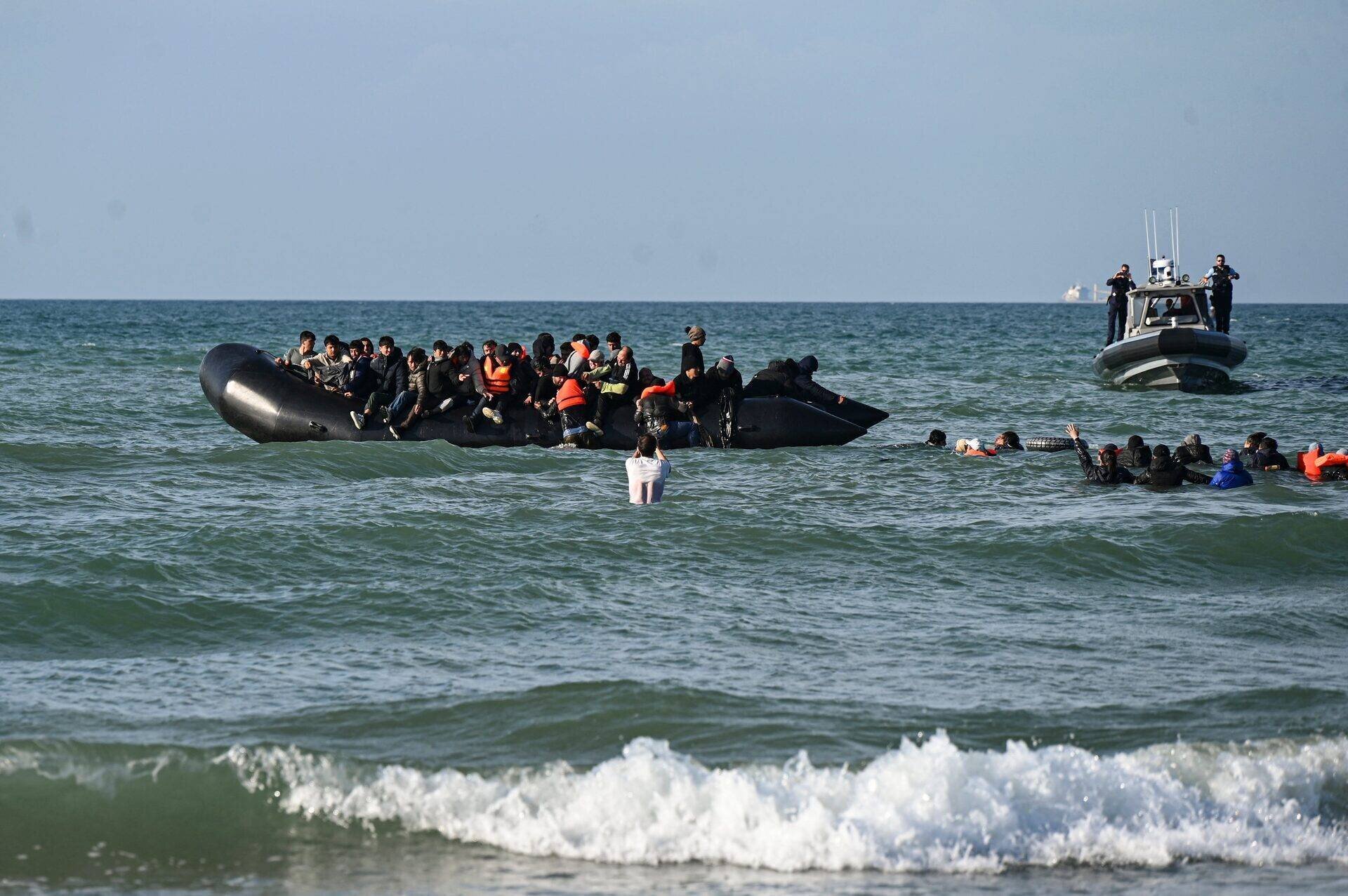 Des migrants nagent pour monter à bord d'un bateau de passeurs sur la plage d'Audresselles, dans le nord de la France, le 25 octobre 2024.