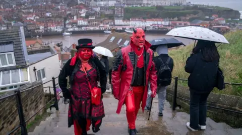 Un homme et une femme avec du maquillage rouge sur le visage et des vêtements gothiques montent les escaliers de Whitby.