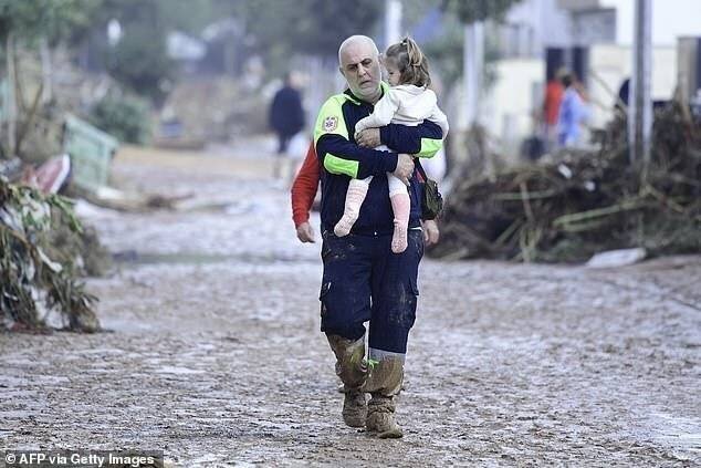 Un membre de la Protection Civile porte un enfant dans une rue inondée.