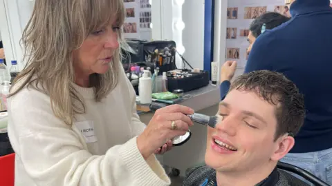 Elliot Caswell se faisant maquiller