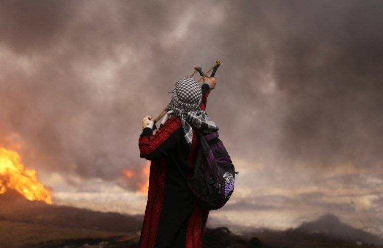 A Palestinian woman uses a slingshot to hurl stones towards Israeli security forces during clashes in tents protest