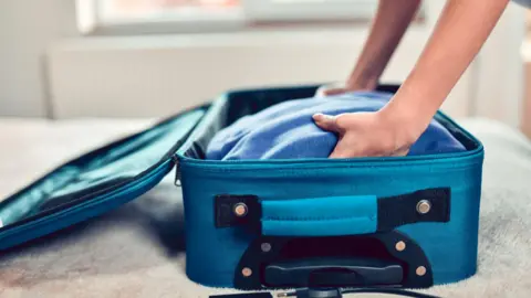 Une personne plaçant un pull dans une valise bleue.