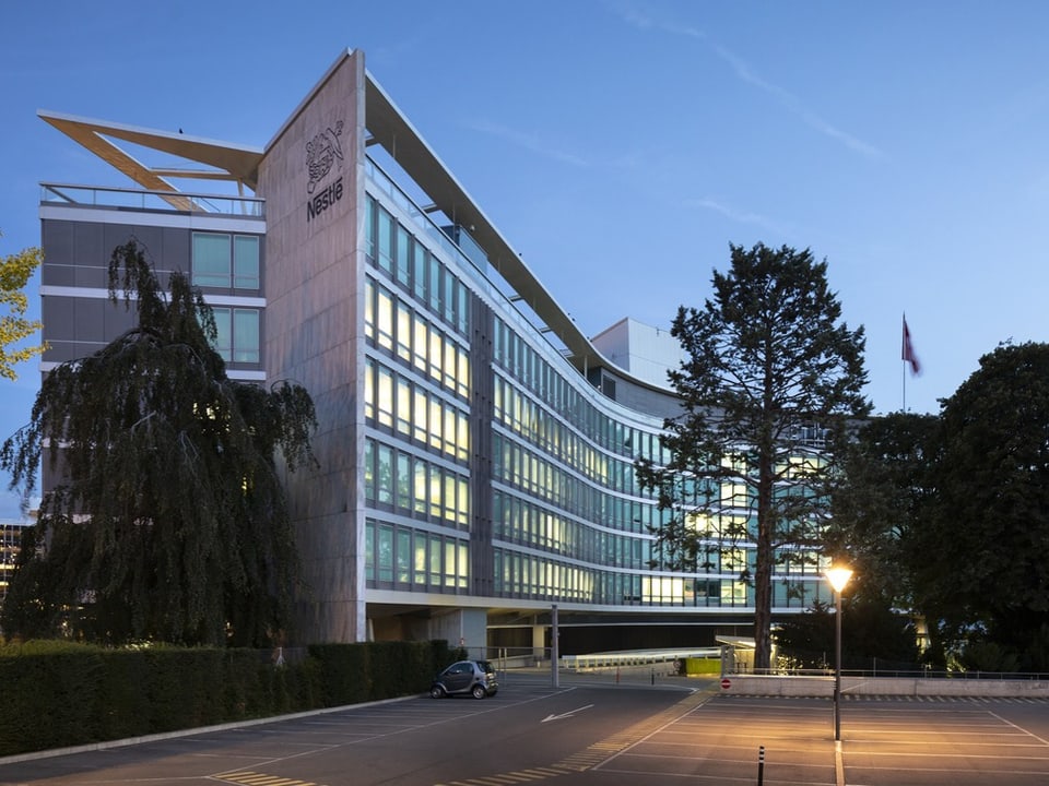 Modernes Gebäude mit Glasfassade und Parkplatz bei Dämmerung.