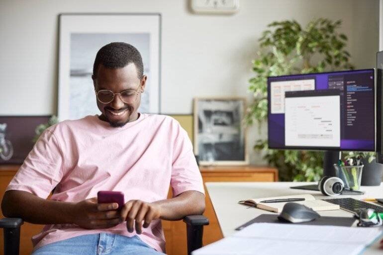 Un homme d'affaires souriant utilisant son téléphone intelligent à son bureau.