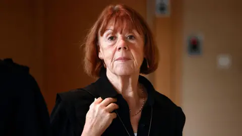 Gisèle Pelicot, une femme aux cheveux roux, regarde la caméra sans sourire.