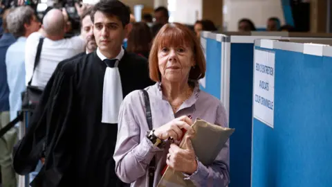 Gisèle Pelicot avec un dossier de documents, suivie par son avocat.