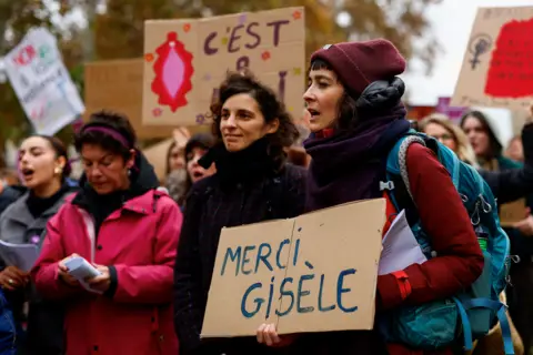 Un groupe de femmes tenant des pancartes en soutien à Gisèle.