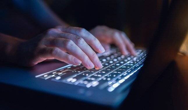 Femme tapant sur un clavier d'ordinateur dans l'obscurité, travaillant tard sur un ordinateur portable chez elle