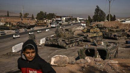 Un jeune garçon devant des tanks abandonnés par l'armée syrienne, à Mankat al-Hatab (Syrie), le 17 décembre 2024. (ARIS MESSINIS / AFP)