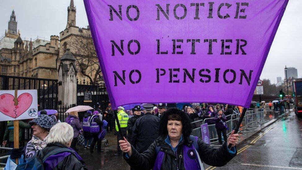 Une militante Waspi tient une bannière violette lors d'une manifestation