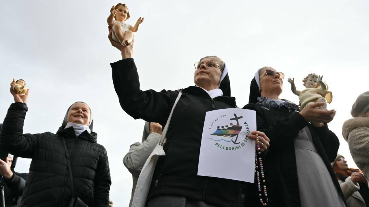 Des religieuses brandissent des figurines de l'enfant Jésus et le logo du Jubilé 2025 lors de la prière de l'Angélus du pape François sur la place Saint-Pierre au Vatican, le 22 décembre 2024.