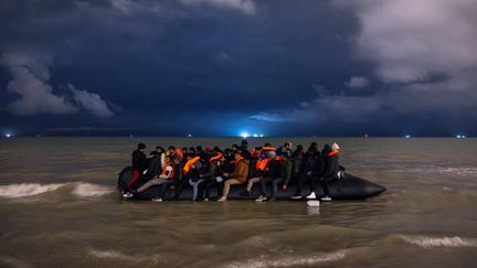 Des migrants montent à bord d'un canot pneumatique de passeurs pour tenter de traverser la Manche, sur la plage Blériot à Sangatte, près de Calais, le 30 octobre 2024. (SAMEER AL-DOUMY / AFP)