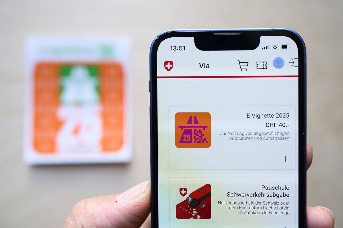 Un homme tient un smartphone avec l'E-Vignette pour l'année 2025, en arrière-plan une vignette autoroutière traditionnelle, photographié à Bern. (KEYSTONE/Christian Beutler)