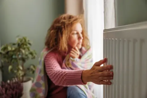 Femme portant un pull et enveloppée dans une couverture près d'un radiateur.
