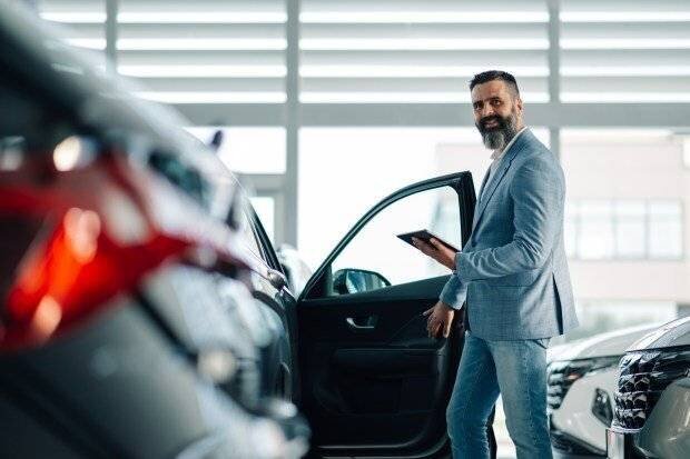 Un homme en costume bleu examine l'intérieur d'une voiture dans un concessionnaire.