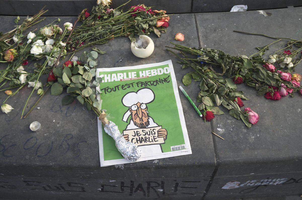 Mémorial sur la Place de la République à Paris avec des fleurs et une édition de Charlie Hebdo intitulée « Tout est pardonné » en mémoire des victimes du terrorisme.