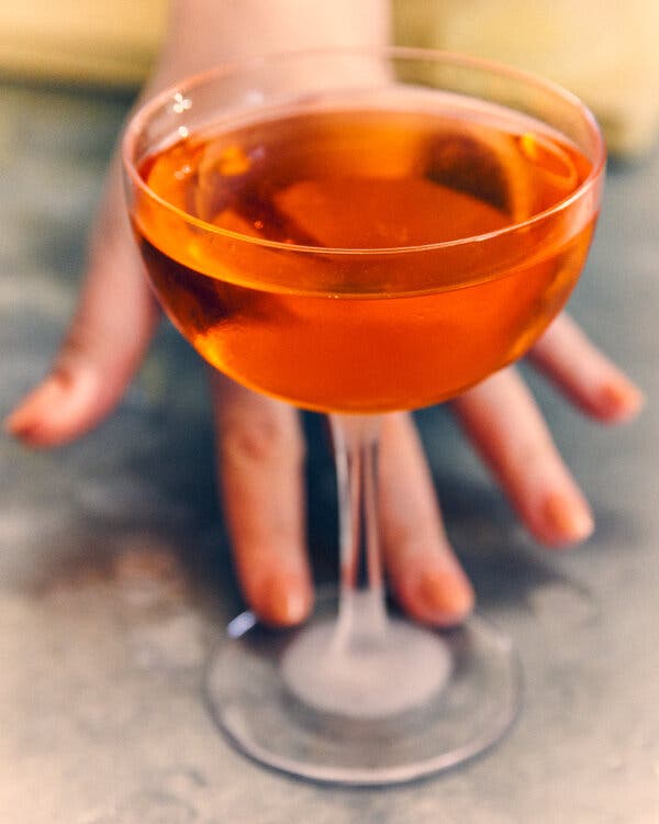Une main manucurée tend vers un verre de cocktail plein.