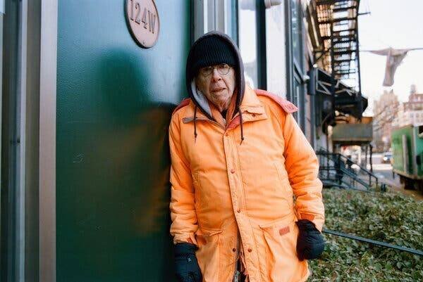 A.J. Weberman devant un bâtiment, vêtu d'un manteau orange et d'un bonnet noir.