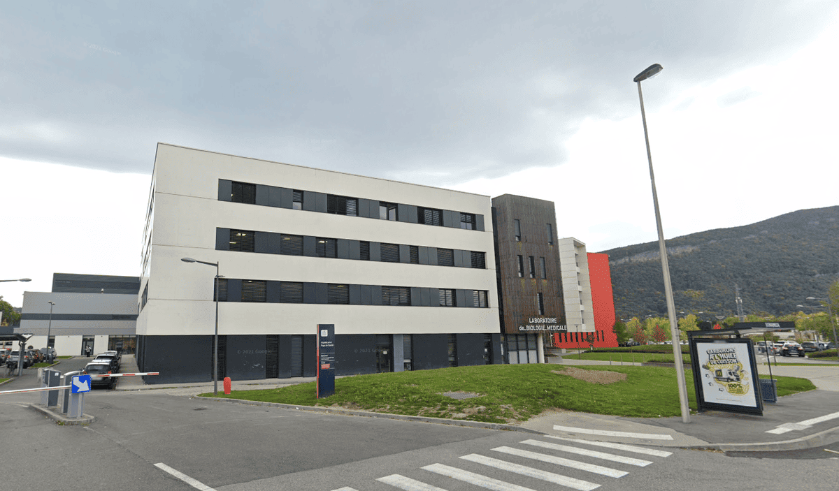 Bâtiment moderne d’une administration sur fond de colline et ciel nuageux, avec un passage piéton au premier plan.