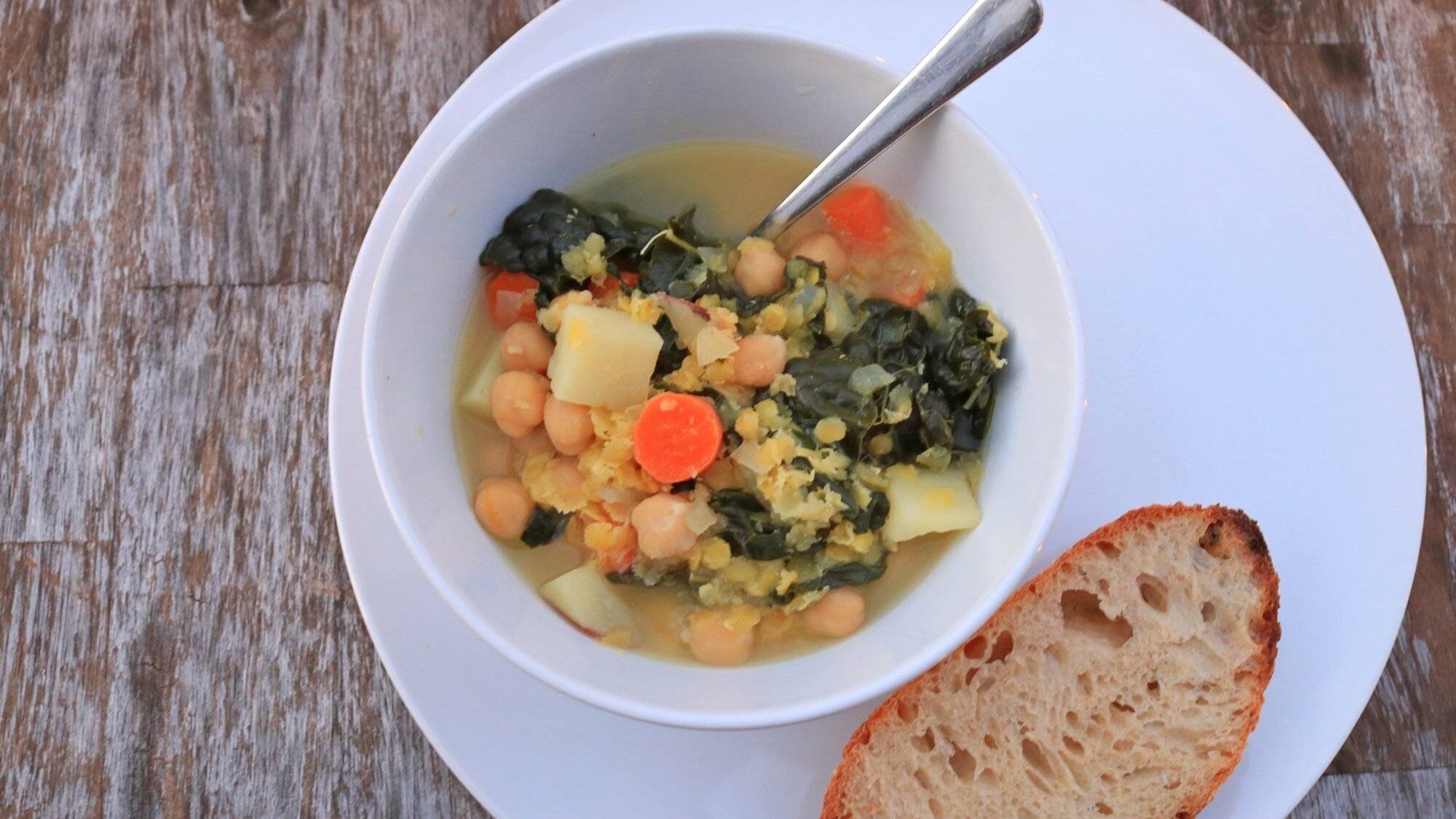 Un bol de soupe de lentilles et de pois chiches avec du pain sur une table.