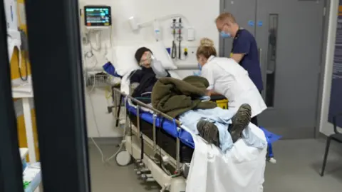 Un patient allongé dans un lit d'hôpital avec des infirmières s'occupant de lui légèrement floues.