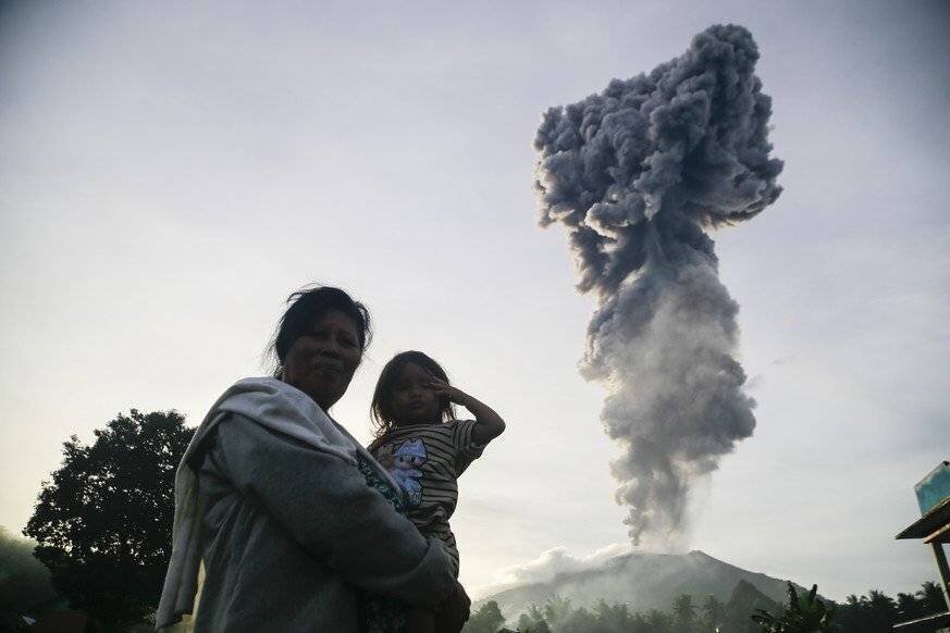 Mount Ibu during the eruption, with a woman carrying a child in the foreground.