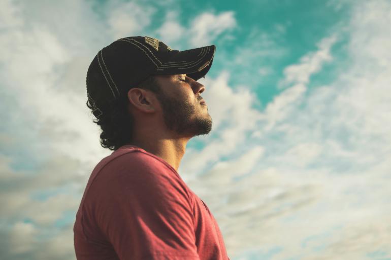 Homme portant une casquette noire avec les yeux fermés sous un ciel nuageux