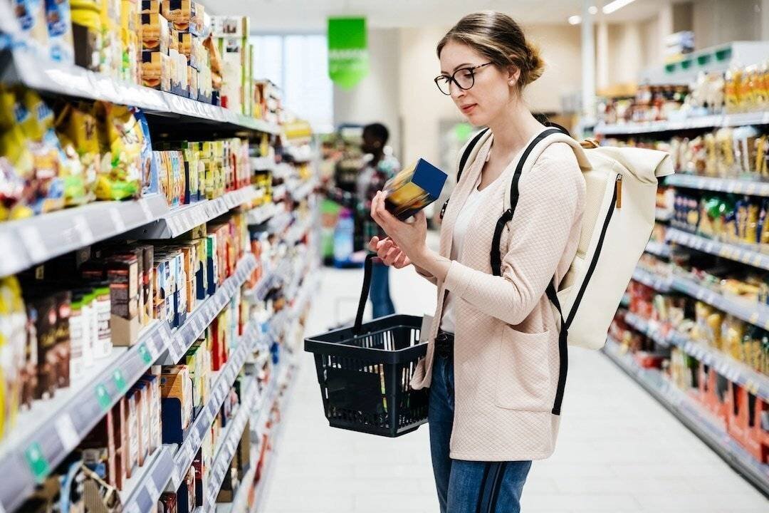 Une femme examine attentivement les ingrédients d'un produit dans un supermarché.
