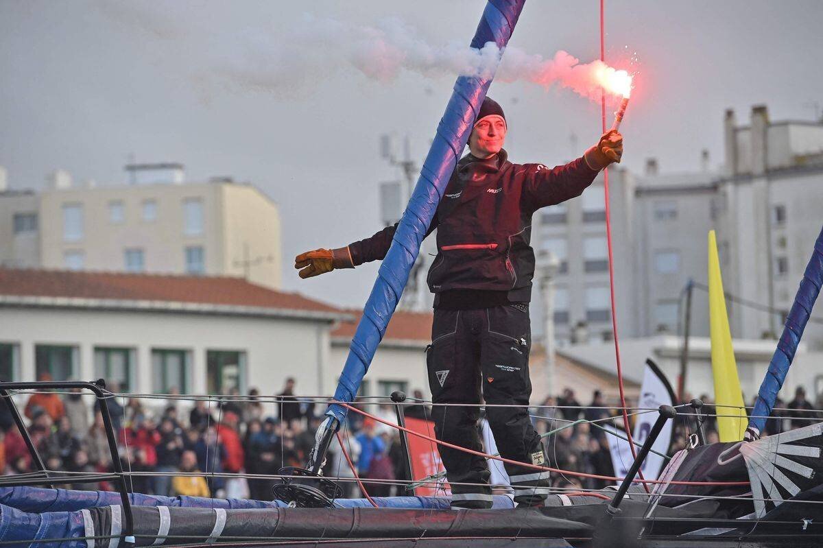 Justine Mettraux tenant un feu à main rouge sur son monocoque Imoca Teamwork, entrant dans le canal aux Sables-d’Olonne après avoir terminé 8e au Vendée Globe.