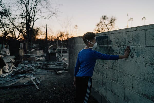 Un petit garçon masqué pose sa main contre le mur d'une école.