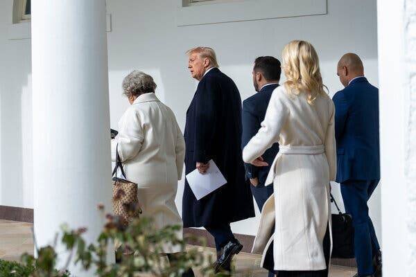 President Trump walking along a colonnade at the White House with members of his staff.