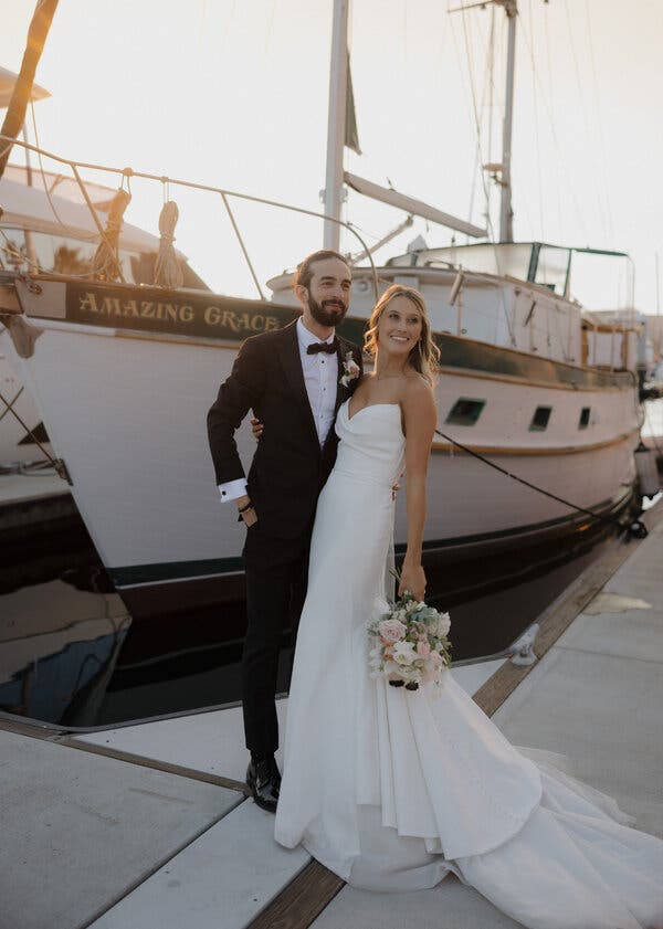 Un couple souriant se tient sur un quai devant un bateau blanc portant le nom 'Amazing Grace'.
