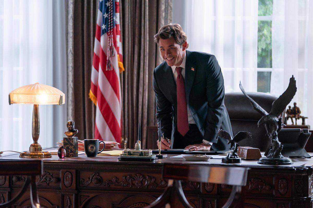 Homme en costume debout derrière un bureau décoré, avec un drapeau américain en arrière-plan et un aigle en métal sur le bureau, scène de «Paradise».