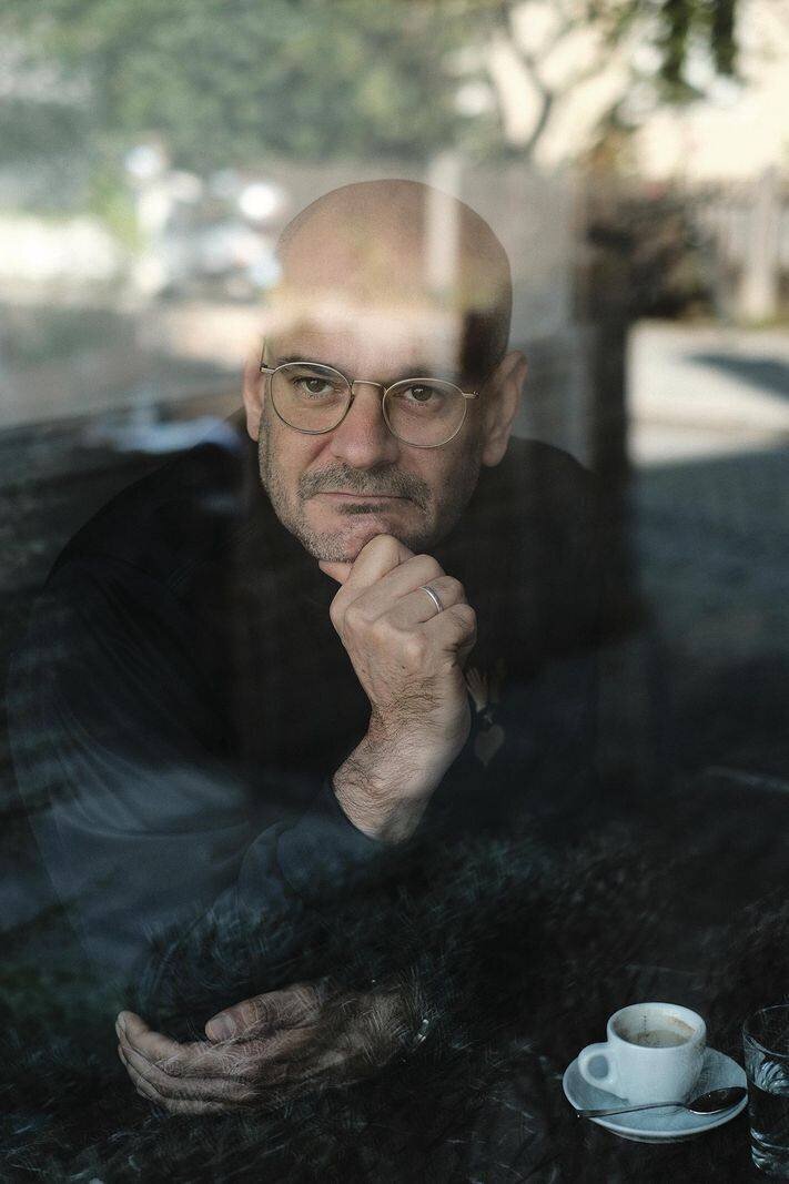 Un homme pensif regardant par une fenêtre, le menton sur sa main avec une tasse de café à côté.