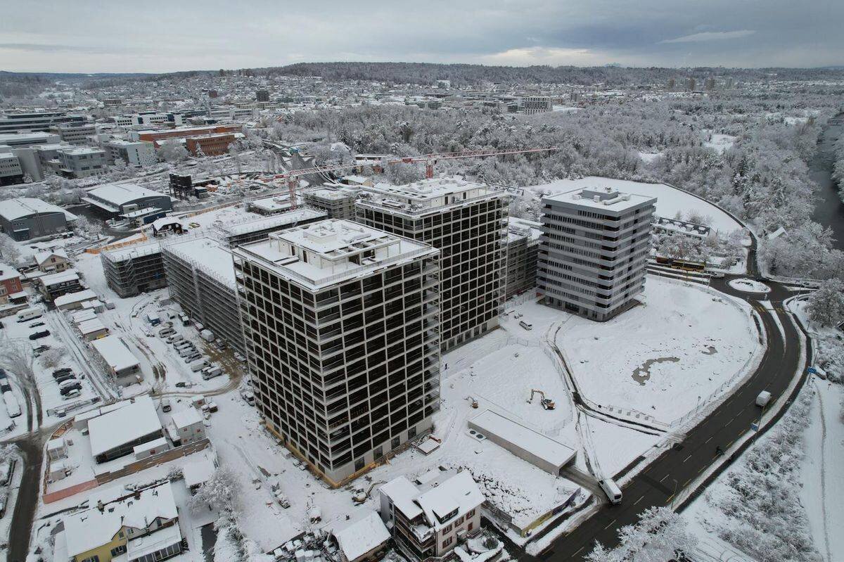 Verschneite Stadtansicht mit grossen Bürogebäuden und schneebedeckter Landschaft im Hintergrund.