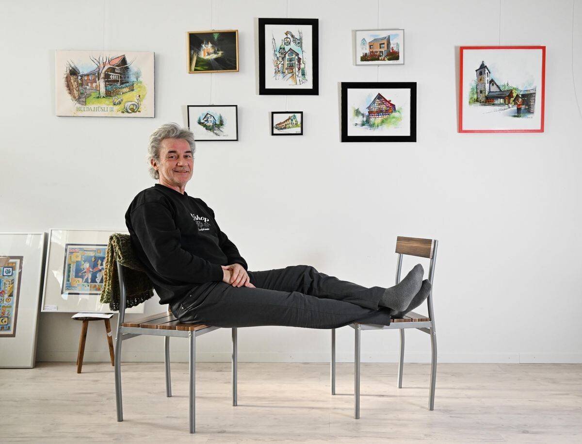 Künstler Stephan Kuhn sitzt entspannt mit den Füssen auf einem Stuhl, umgeben von Urban-Sketching-Kunstwerken in seinem Atelier.