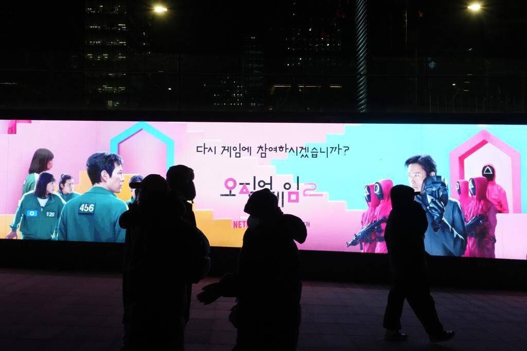 Des passants devant un écran promouvant la série sud-coréenne de Netflix 'Squid Game Saison 2' à Gwanghwamun Square à Séoul, Corée du Sud.