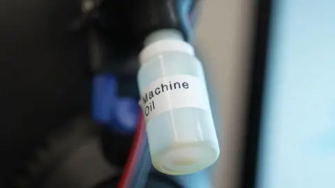 Des bouteilles transparentes attachées à une machine étiquetée 'Machine Oil'.