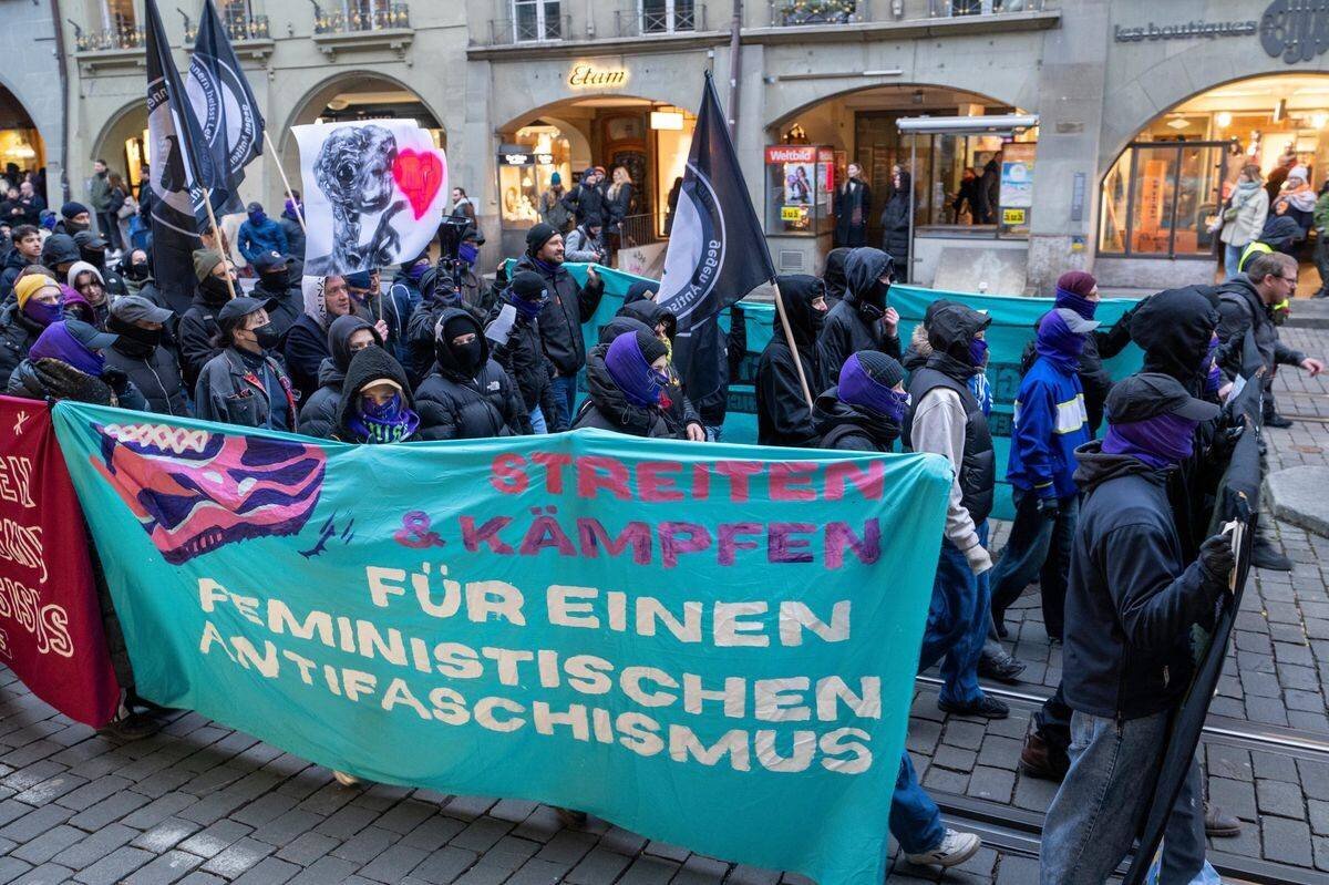 Manifestation à Berne avec des participants portant un drapeau avec des messages féministes et antifascistes.