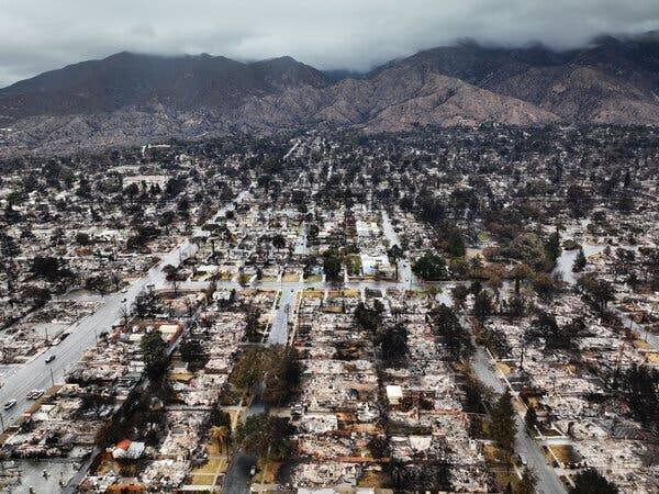 Vue aérienne de plusieurs quartiers de maisons et commerces carbonisés, avec des collines en arrière-plan.