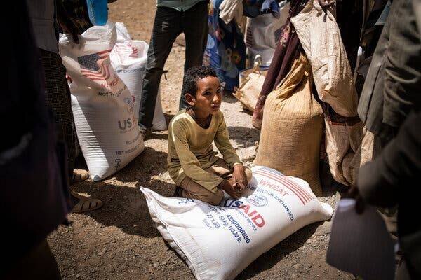 Un jeune garçon à genoux sur un sac de blé avec 'U.S.A.I.D.' écrit dessus.