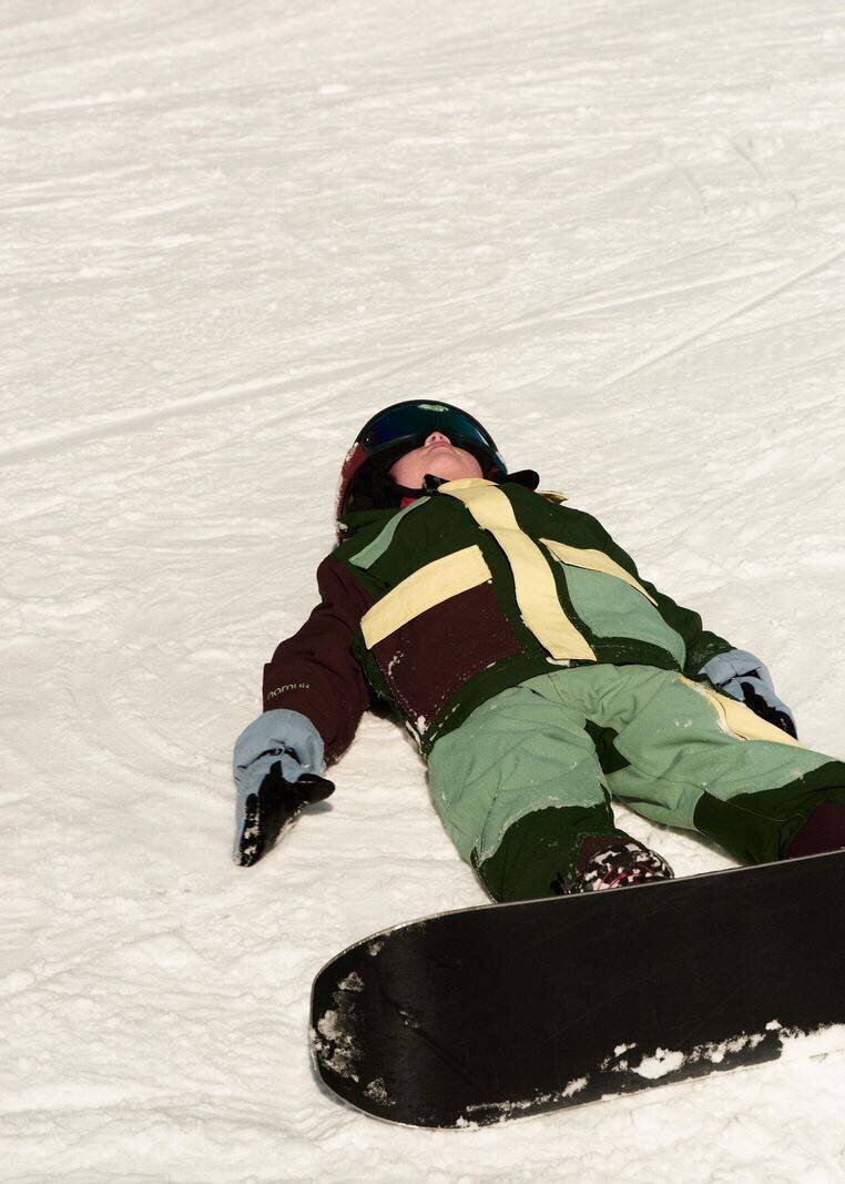 Personne en vêtements d'hiver colorés se trouve dans la neige avec un snowboard.