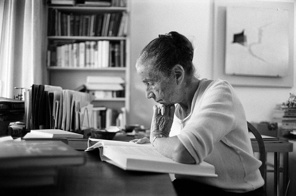 Une femme âgée lisant un livre, entourée de livres.