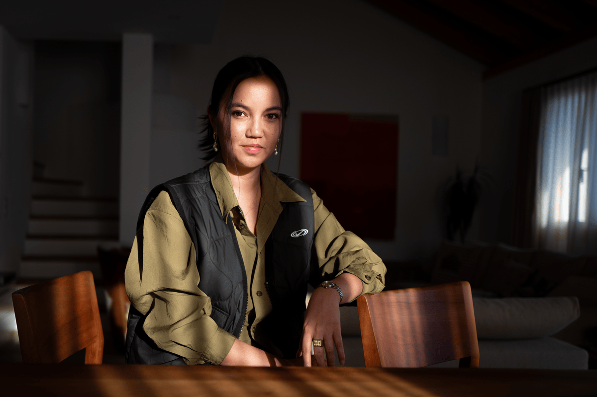 Jessica Rees, une femme assise dans une pièce lumineuse, portant une chemise olive et un gilet noir, regardant vers la caméra.