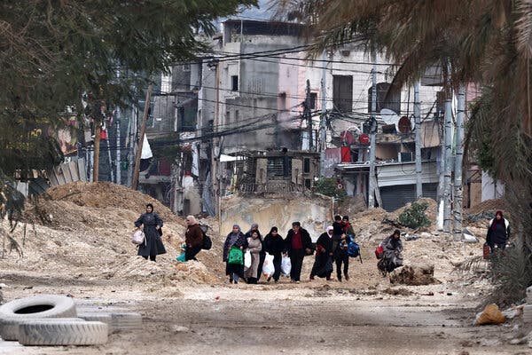 Des Palestiniens portant des sacs avec leurs affaires marchent le long d'une route pendant un raid israélien.