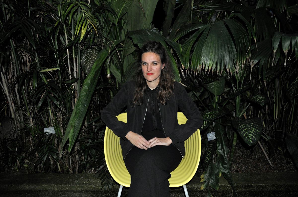 Femme assise sur une chaise jaune entourée de verdure.