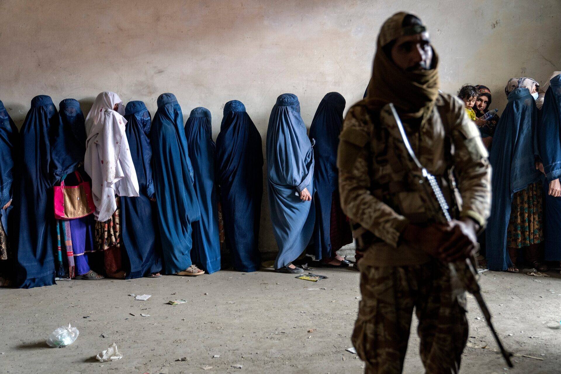 Un combattant taliban surveille alors que des femmes attendent des rations alimentaires à Kaboul, Afghanistan.