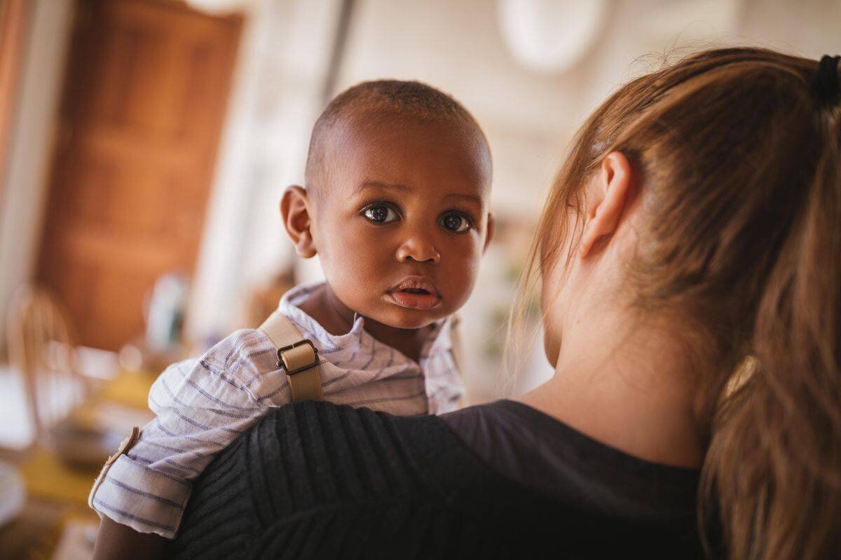 Loving young mother holding with affection adopted African American child at home