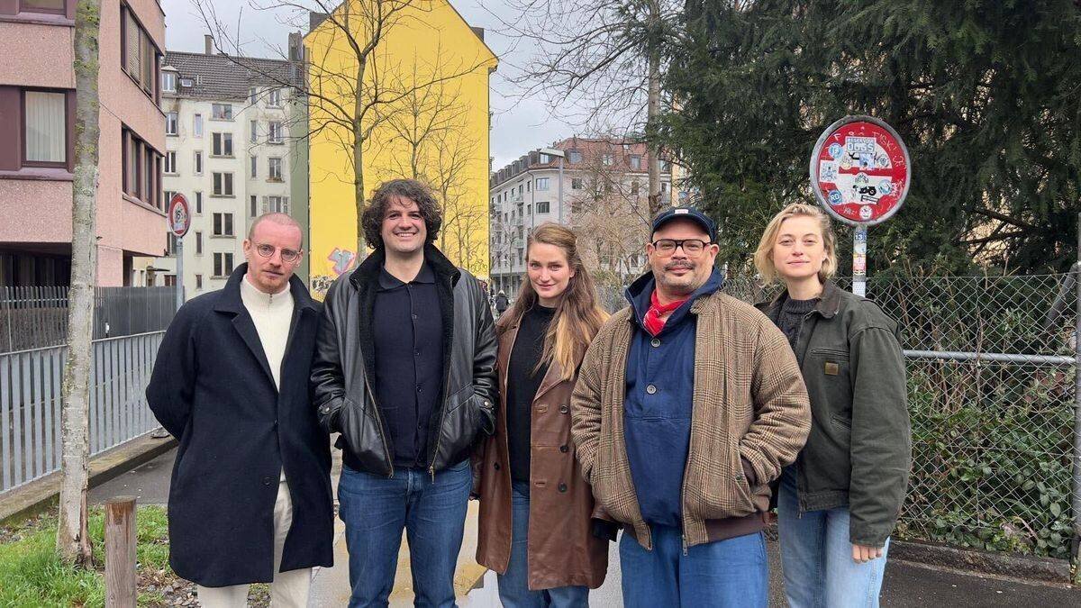 Cinq personnes sur une rue de Zurich, avec des bâtiments colorés en arrière-plan.